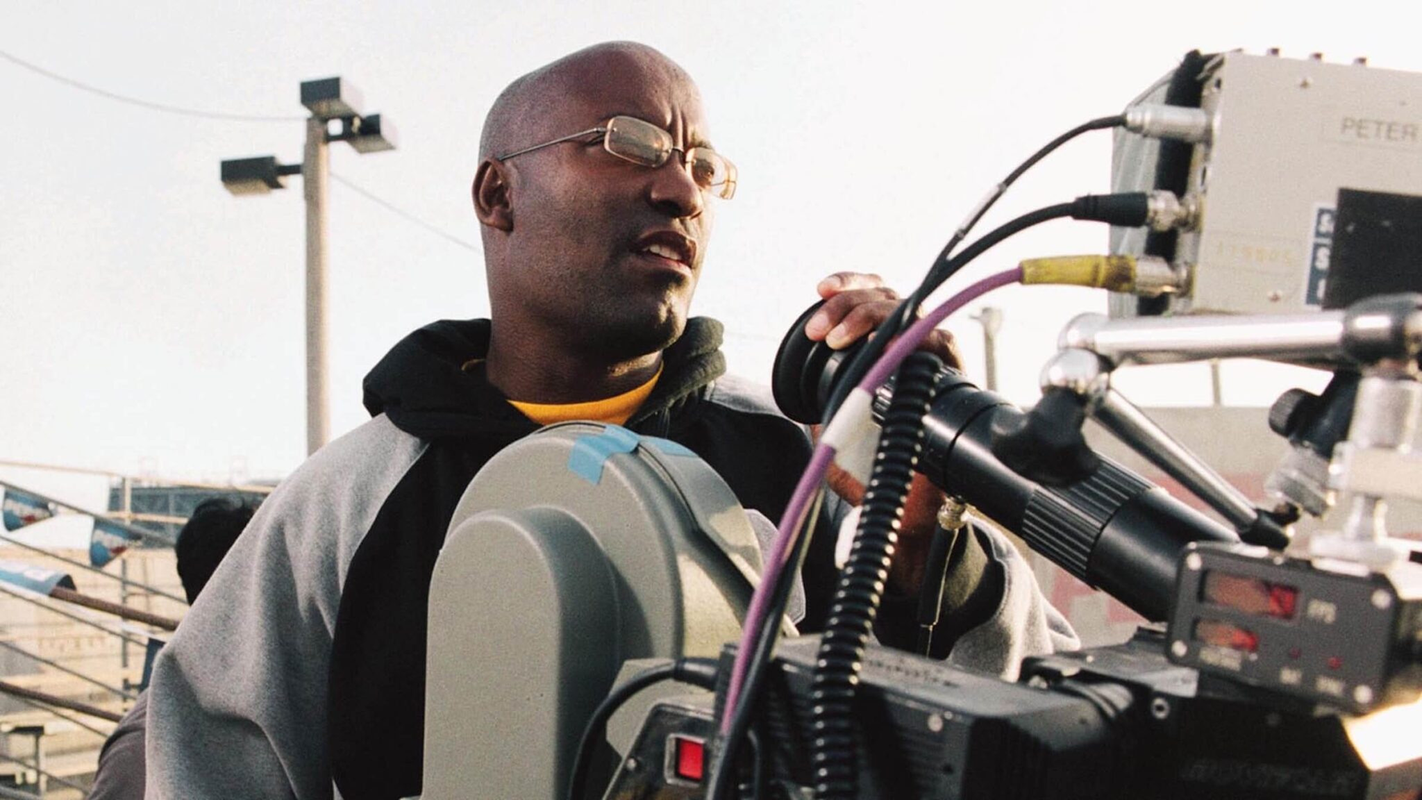 John Singleton directing behind a camera on the set of a film